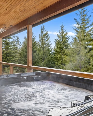 Covered deck with hot tub overlooking forested mountain landscape and blue sky