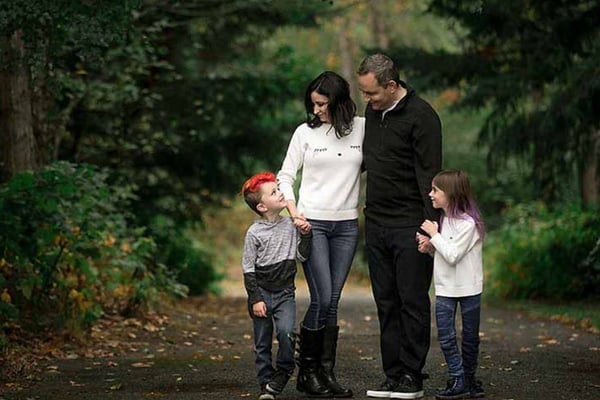 Family of four walking together on a tree-lined path, parents with two young children